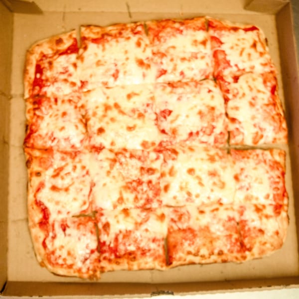 A rectangular cheese pizza, cut into squares, sits inside a cardboard delivery box.