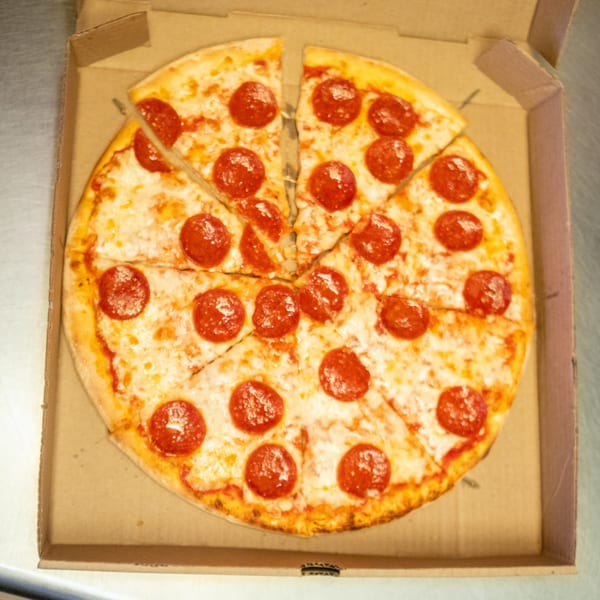 A whole pepperoni pizza, cut into slices, sits in an open cardboard delivery box.