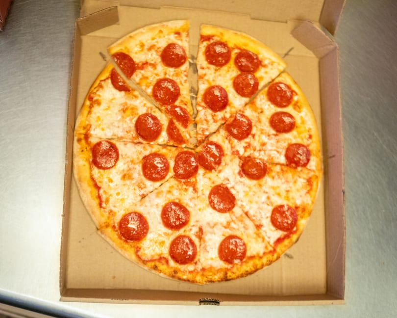A whole pepperoni pizza, cut into slices, sits in an open cardboard delivery box.