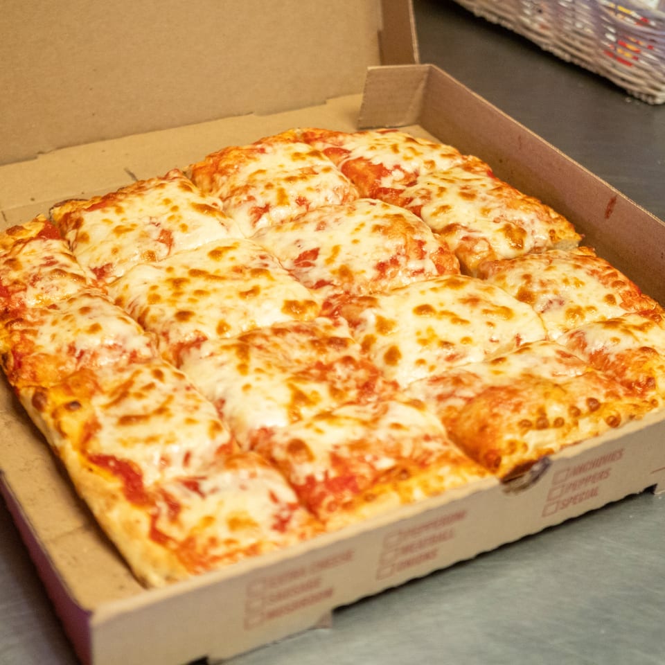 A square cheese pizza, cut into many small squares, sits in an open cardboard box.