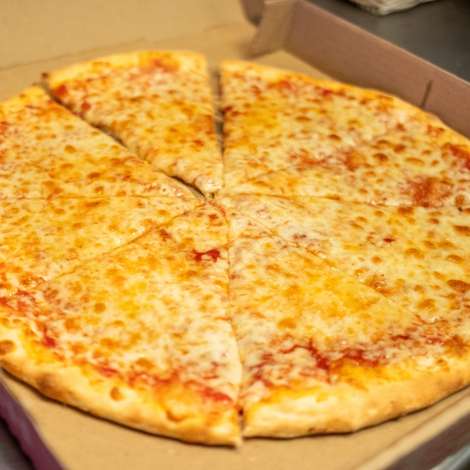 A whole cheese pizza, cut into eight slices, sits in an open cardboard delivery box.