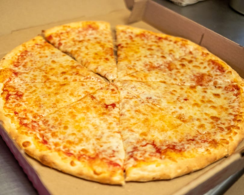 A whole cheese pizza, cut into eight slices, sits in an open cardboard delivery box.