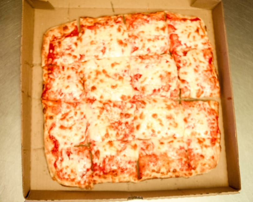 A rectangular cheese pizza, cut into squares, sits inside a cardboard delivery box.